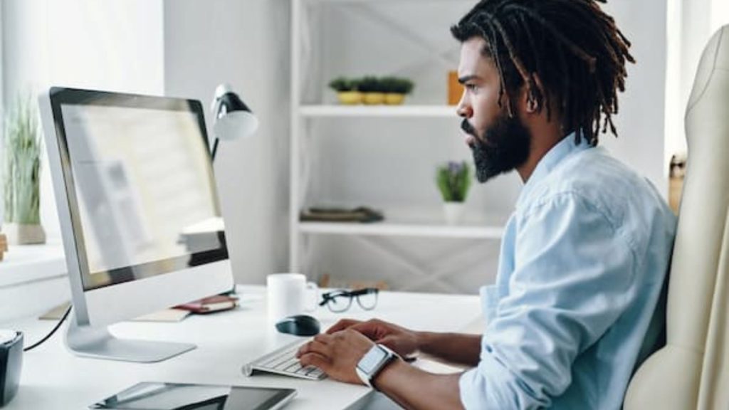 A picture of a dark skin man with Long hair operating a desk top
